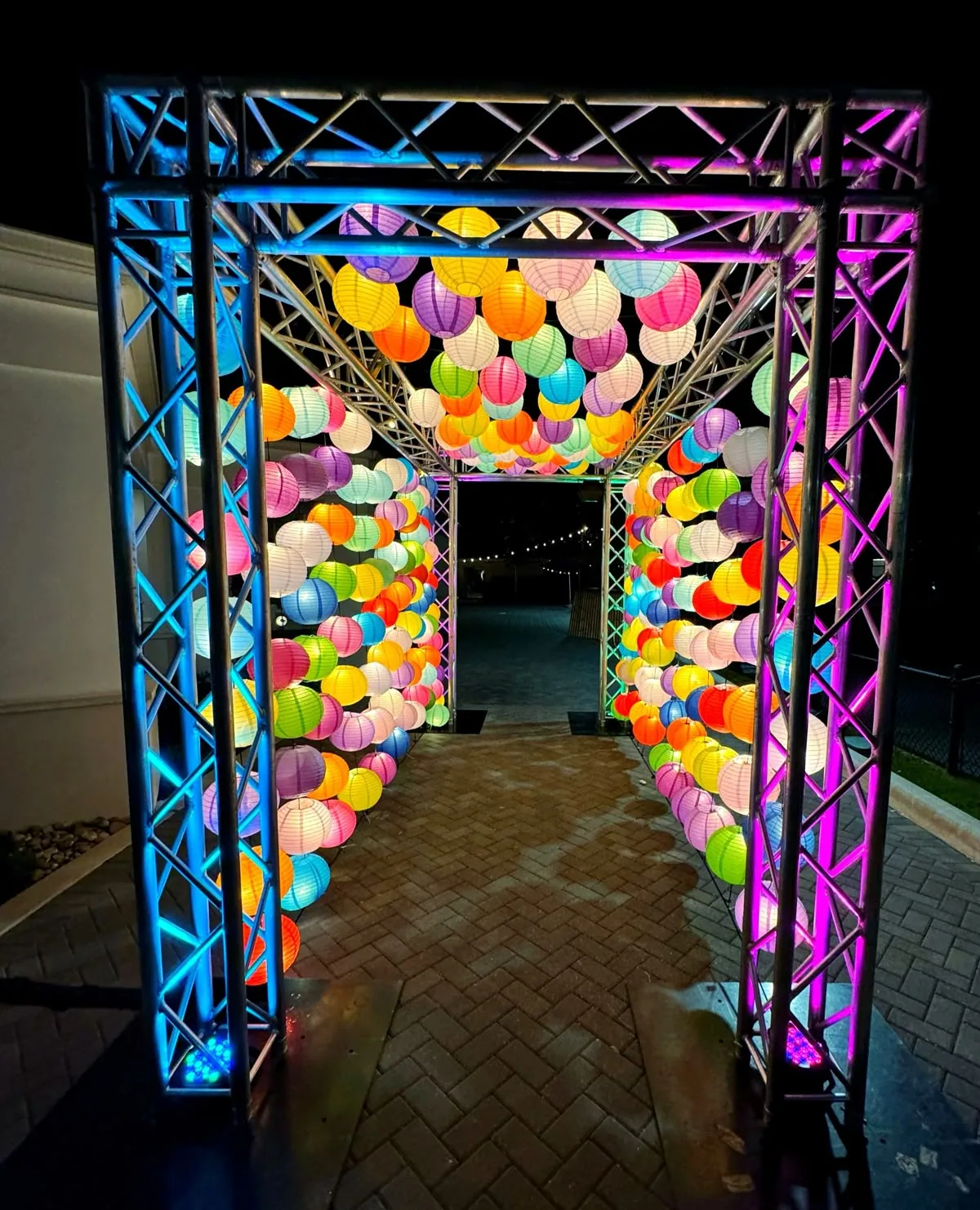Entry gate tunnel of coloured paper lanterns on a lit truss frame at night — event by Plan With YOLO, Pune